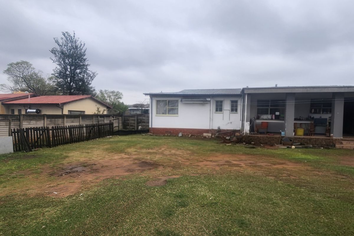 Rear view of the property featuring a spacious backyard, a covered patio area, and perimeter boundary walling.