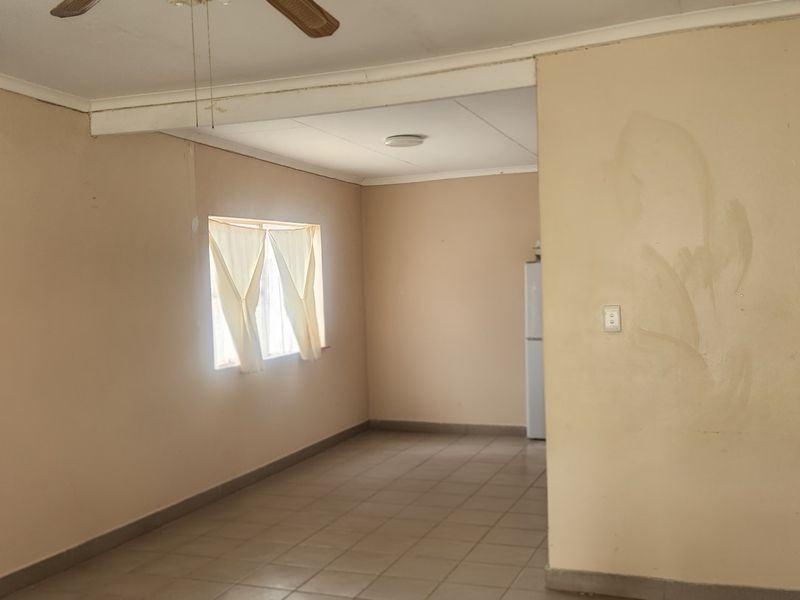 An open-plan living area featuring tiled flooring, a ceiling fan, and neutral wall finishes, currently vacant and ready for renovation.