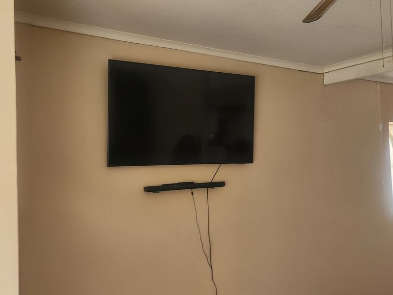 A living room area featuring a wall-mounted television, soundbar, and ceiling fan, providing a functional space ready for personalization.