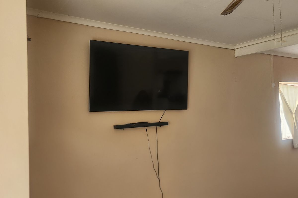 A living room area featuring a wall-mounted television, soundbar, and ceiling fan, providing a functional space ready for personalization.