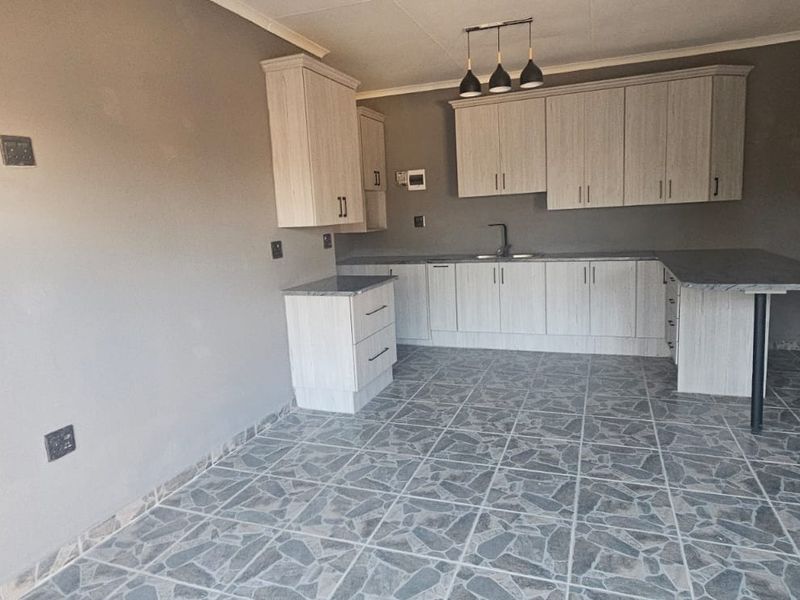 A modern, empty kitchen featuring light wood-grain cabinetry, stone-look tiled flooring, and a functional breakfast bar layout.