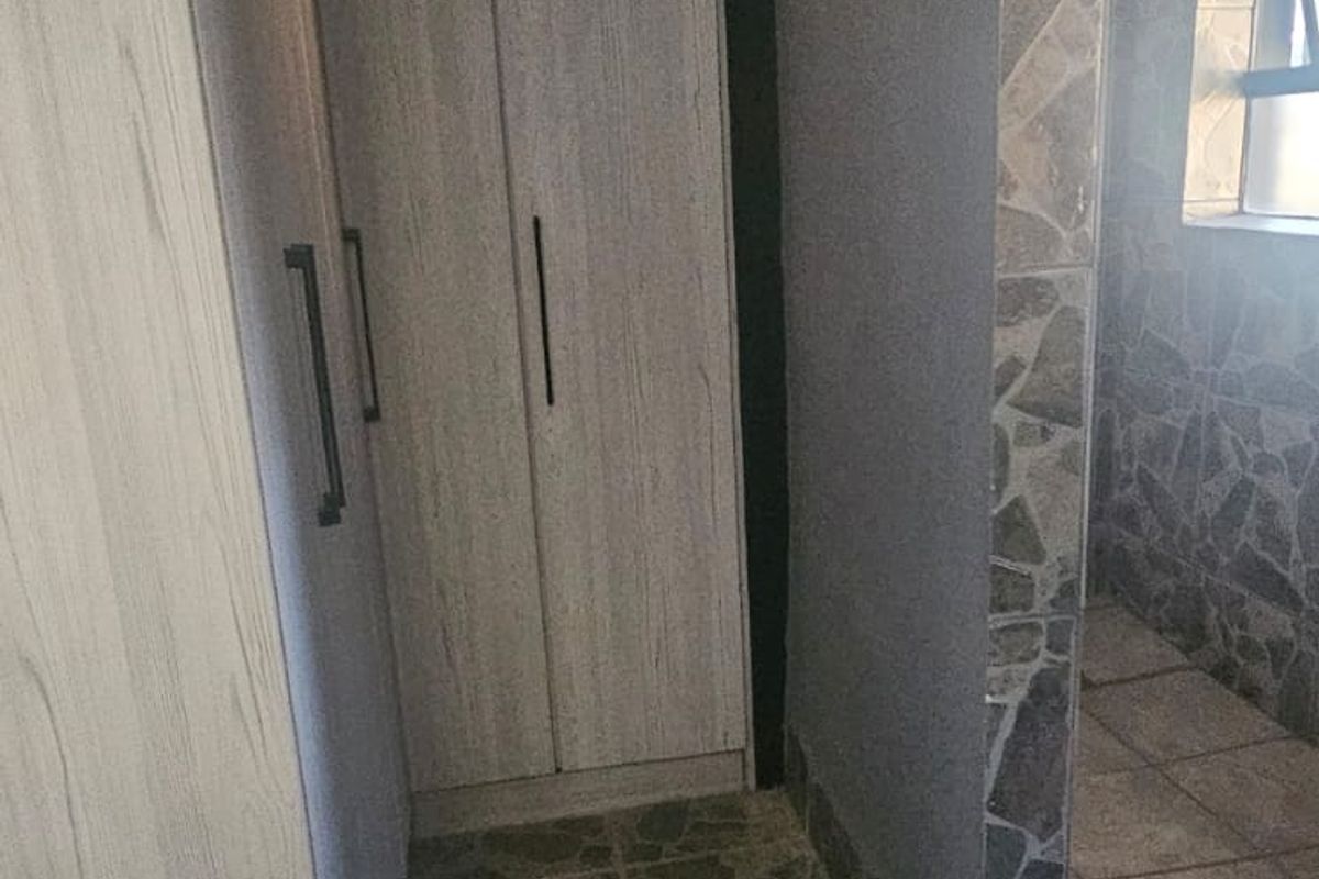 A bedroom area featuring built-in cupboards, stone-cladding wall accents, and tiled flooring.