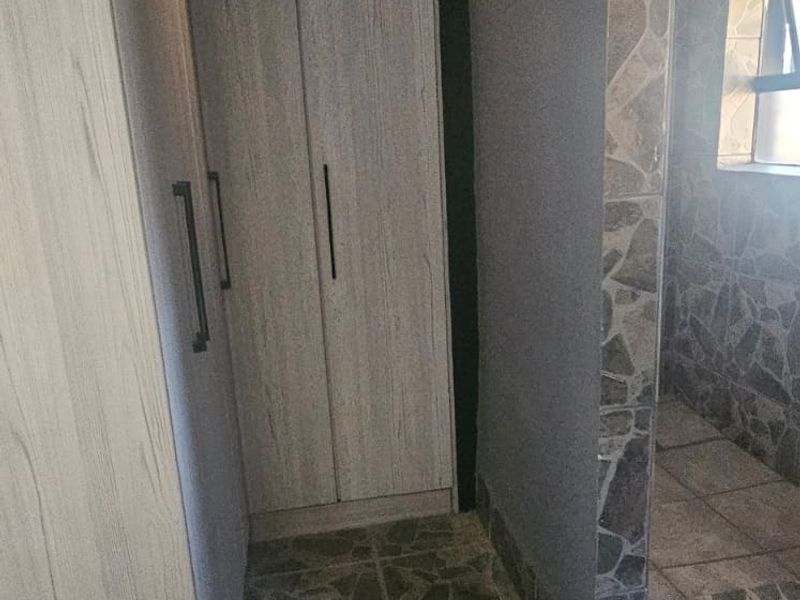 A bedroom area featuring built-in cupboards, stone-cladding wall accents, and tiled flooring.