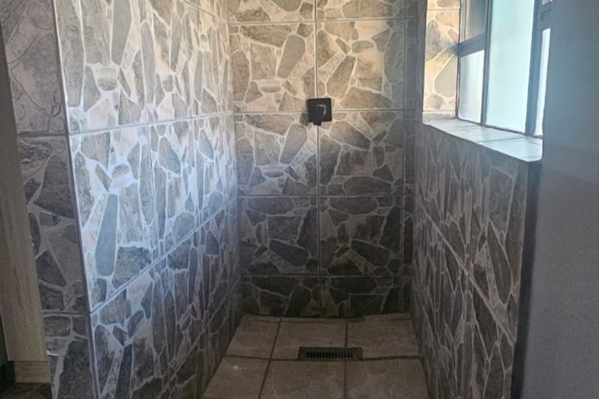 A walk-in shower featuring stone-style wall tiling, a modern rain shower head, and a linear floor drain with a side window.