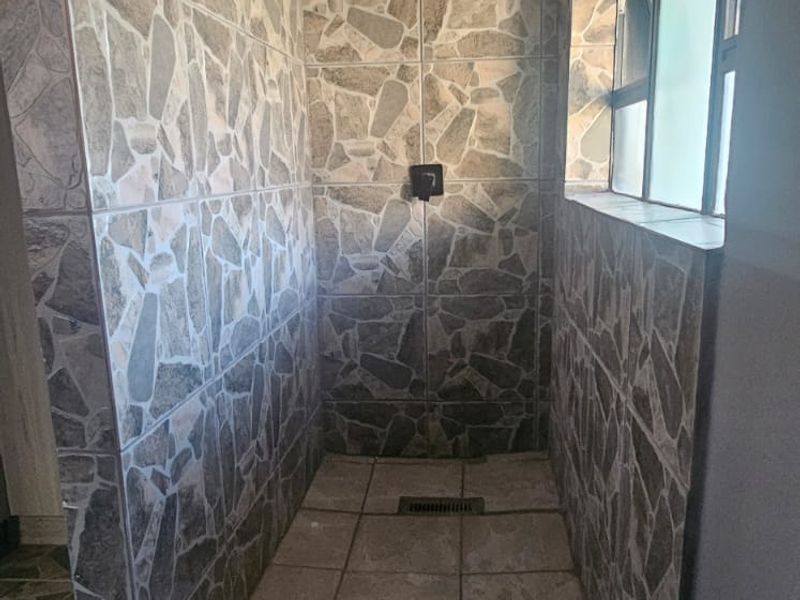 A walk-in shower featuring stone-style wall tiling, a modern rain shower head, and a linear floor drain with a side window.