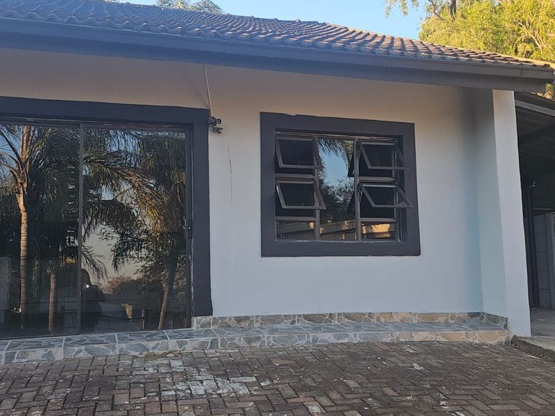Rear exterior view of the cottage featuring a paved patio area, sliding glass doors, top-hung windows, and an attached carport structure.