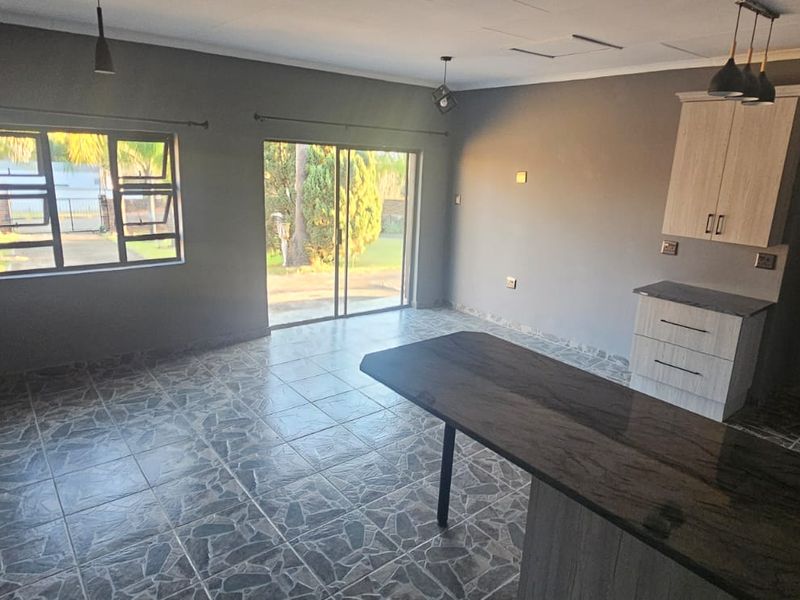 Open-plan living and kitchen area featuring tiled flooring, modern cabinetry with granite countertops, and direct access to the garden through sliding glass doors.