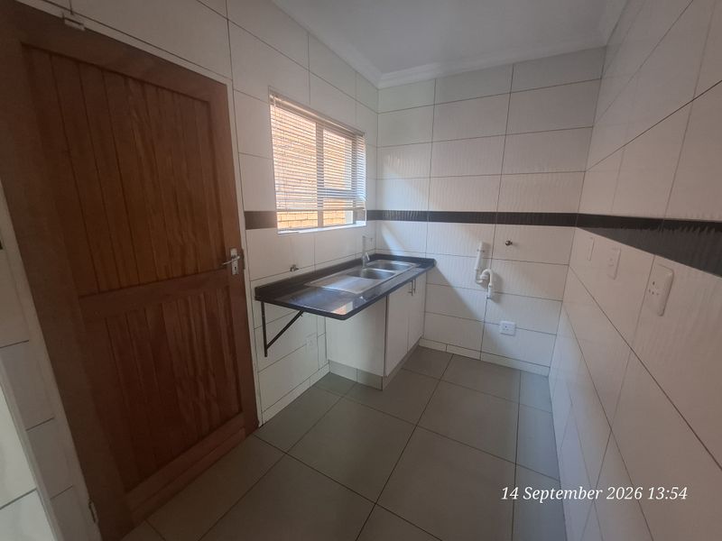 A functional laundry room featuring tiled walls, a double sink with a dark countertop, and dedicated plumbing connections for appliances.