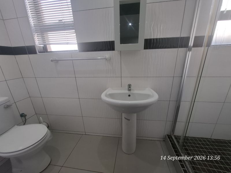 A clean, functional bathroom featuring a pedestal basin, toilet, and a glass-enclosed shower with modern tiled finishes.