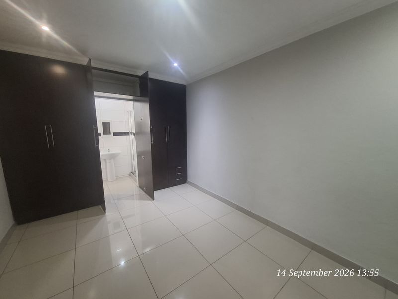 A clean, empty bedroom featuring tiled flooring, built-in dark wood cupboards, and direct access to an en-suite bathroom.