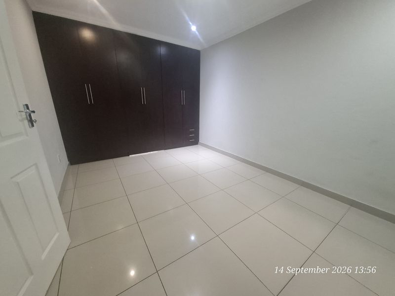 A clean, empty bedroom featuring neutral tiled flooring and dark wood built-in cupboards, providing a versatile space ready for furnishing.