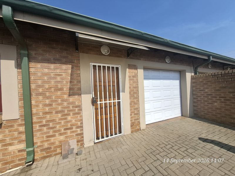 Exterior view of a townhouse garage featuring a white sectional door, a secure pedestrian entrance, and paved driveway area.
