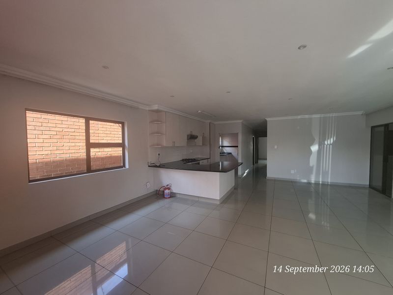 Spacious open-plan living and kitchen area featuring tiled flooring, modern cabinetry with granite countertops, and recessed lighting in a clean, vacant setting.