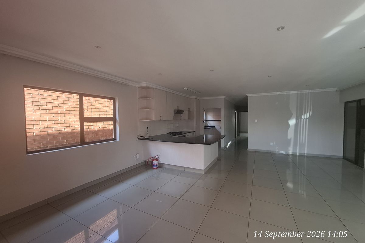 Spacious open-plan living and kitchen area featuring tiled flooring, modern cabinetry with granite countertops, and recessed lighting in a clean, vacant setting.