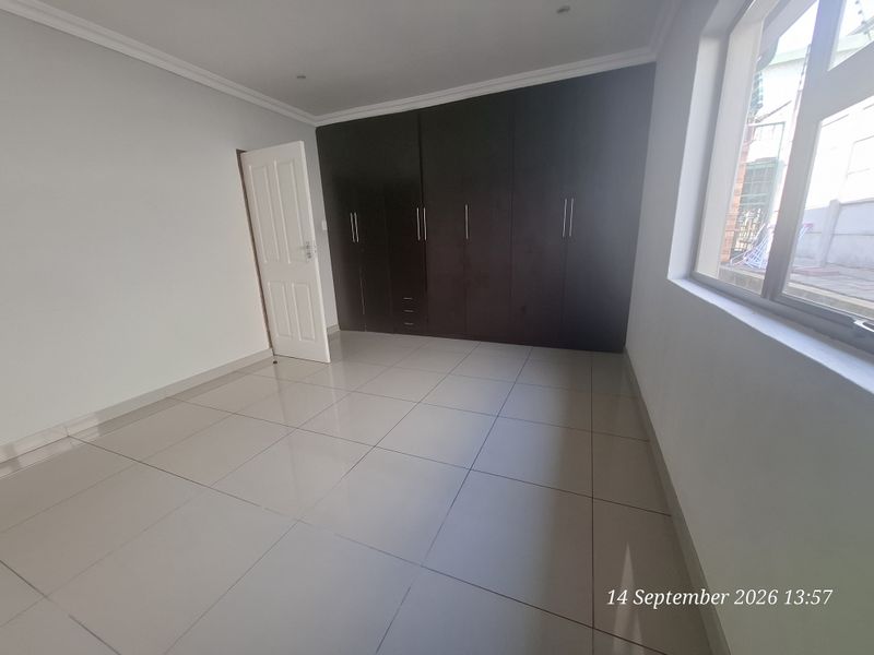 A bright, empty bedroom featuring neutral tiled flooring, recessed ceiling lights, and dark wood built-in cupboards providing ample storage space.