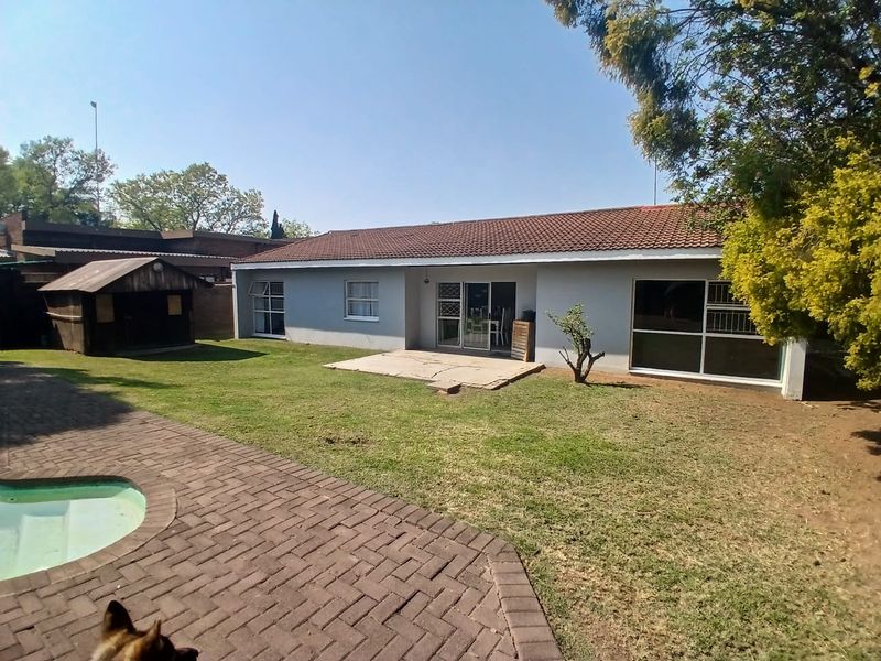 Rear view of the house featuring a tiled roof, sliding glass doors, a paved patio area, and a swimming pool set in a garden.