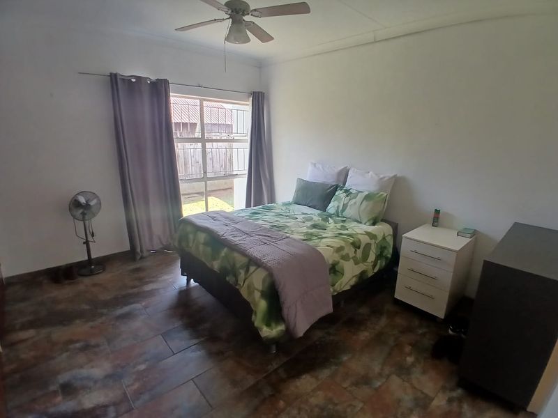 A bedroom featuring tiled flooring, a ceiling fan, and a window with security bars, providing a functional and well-lit living space.