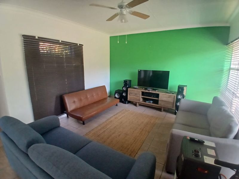 A living room featuring tiled flooring, a ceiling fan, and window blinds, with a prominent green accent wall.