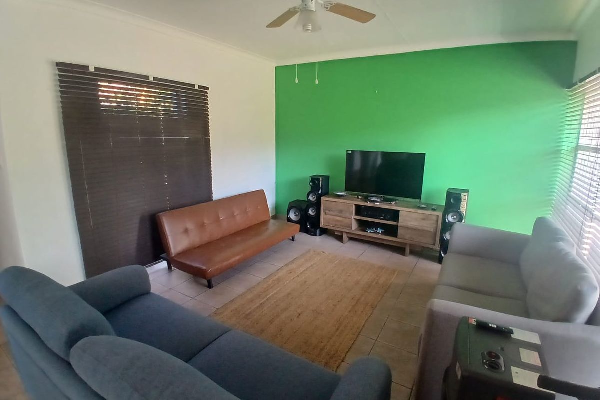 A living room featuring tiled flooring, a ceiling fan, and window blinds, with a prominent green accent wall.