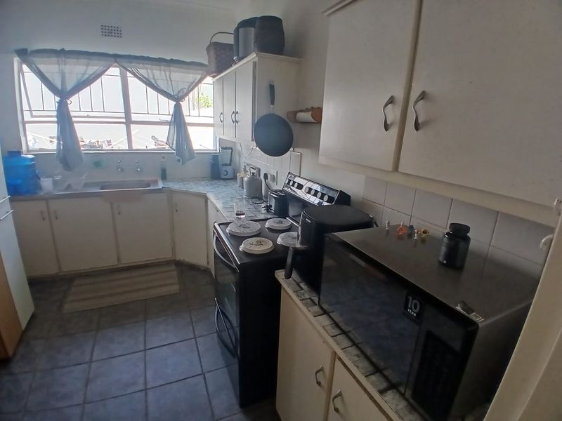 A functional kitchen featuring built-in cabinetry, tiled flooring, and a tiled backsplash, offering a practical layout with potential for modern cosmetic updates.