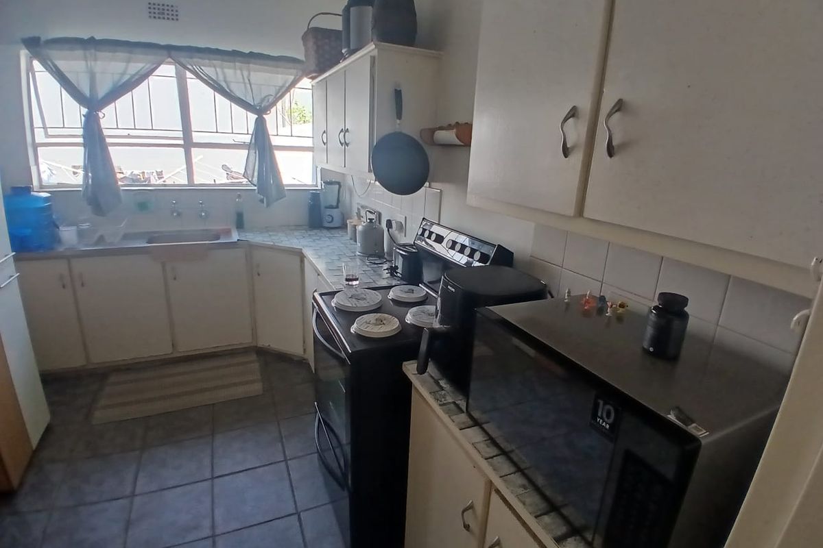 A functional kitchen featuring built-in cabinetry, tiled flooring, and a tiled backsplash, offering a practical layout with potential for modern cosmetic updates.