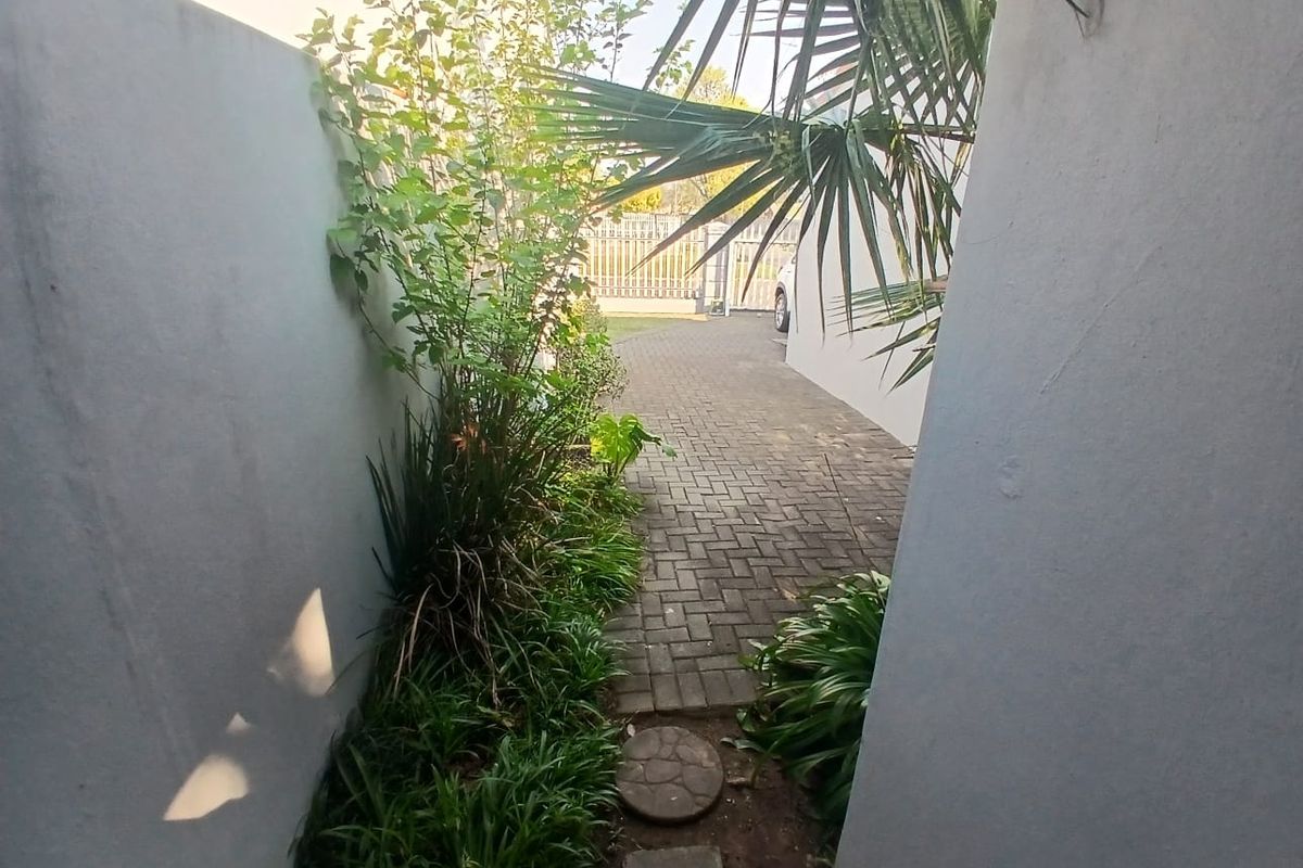 A narrow side pathway featuring paved brickwork, boundary walls, and established garden greenery leading towards the rear driveway area.