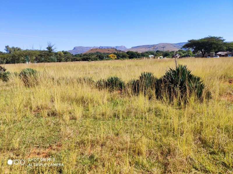 A wide-angle view of a vacant residential plot featuring natural grassland and distant mountain scenery.
