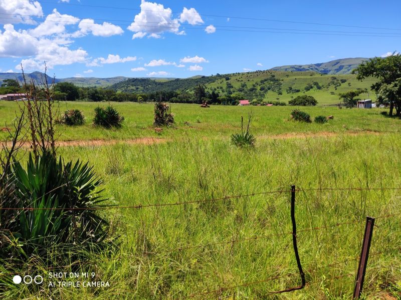 A scenic view of an expansive, grassy vacant residential plot with rolling hills in the background and a perimeter wire fence.