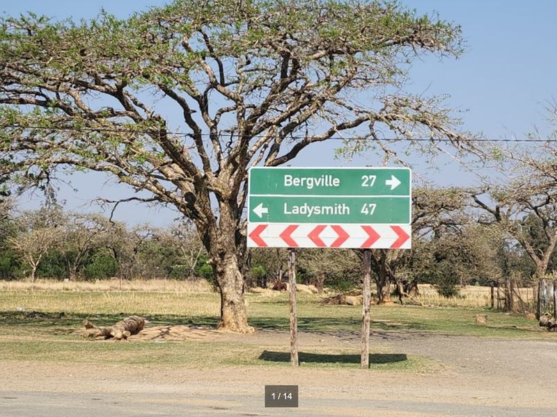 A roadside view showing a directional sign indicating distances to Bergville and Ladysmith, set against a backdrop of open vacant land.