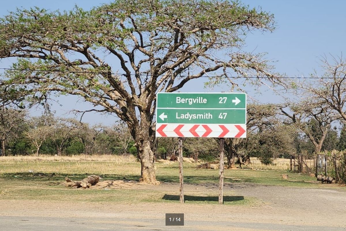 A roadside view showing a directional sign indicating distances to Bergville and Ladysmith, set against a backdrop of open vacant land.