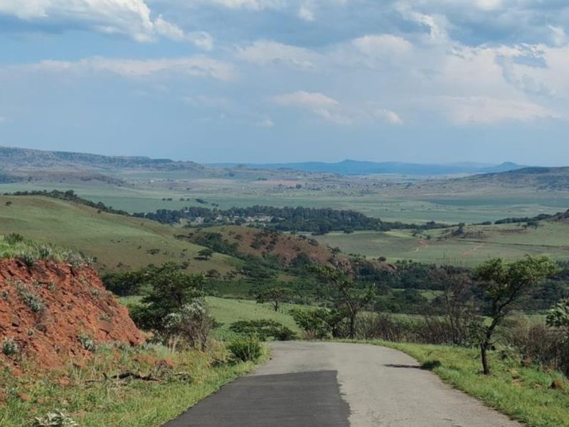 A scenic view of the surrounding rural landscape and rolling hills, featuring an asphalt access road leading through the property.