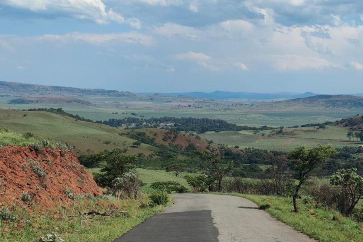 A scenic view of the surrounding rural landscape and rolling hills, featuring an asphalt access road leading through the property.