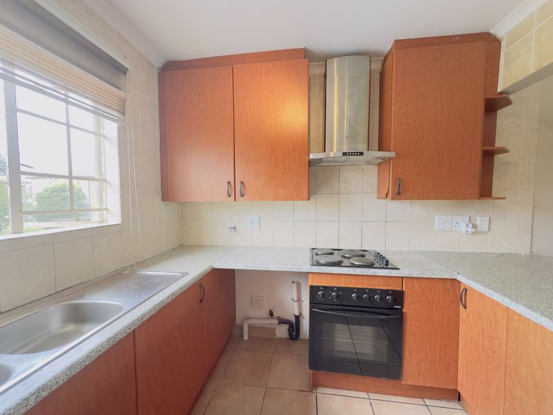 A functional kitchen featuring wood-look cabinetry, laminate countertops, a built-in oven with hob, and a stainless steel extractor fan.