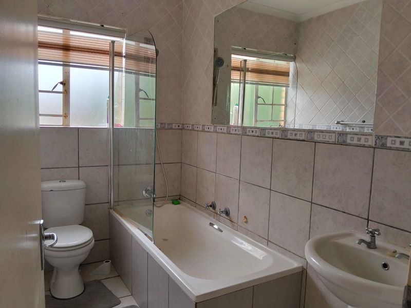 A functional bathroom featuring a bathtub with a glass screen, pedestal basin, and tiled finishes, offering a clean and practical layout.