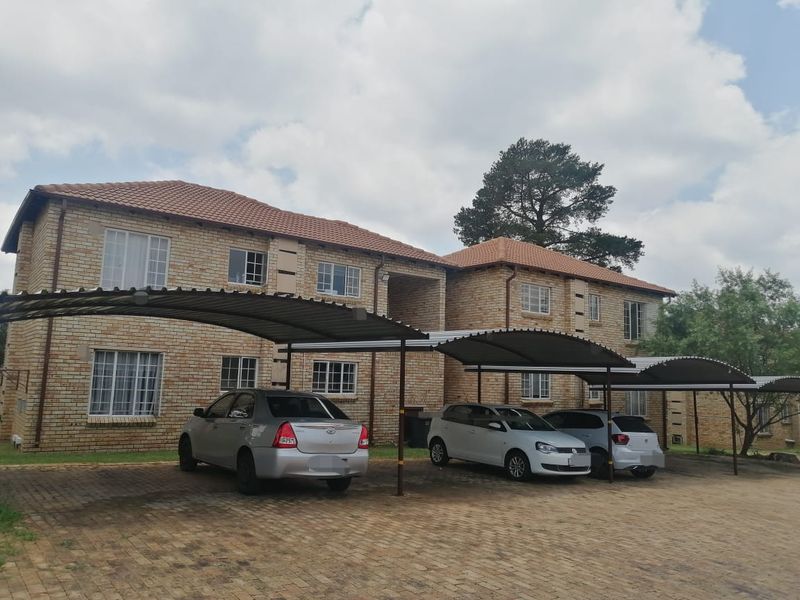 Front elevation of a face brick townhouse complex featuring covered carport parking bays and a paved driveway area.
