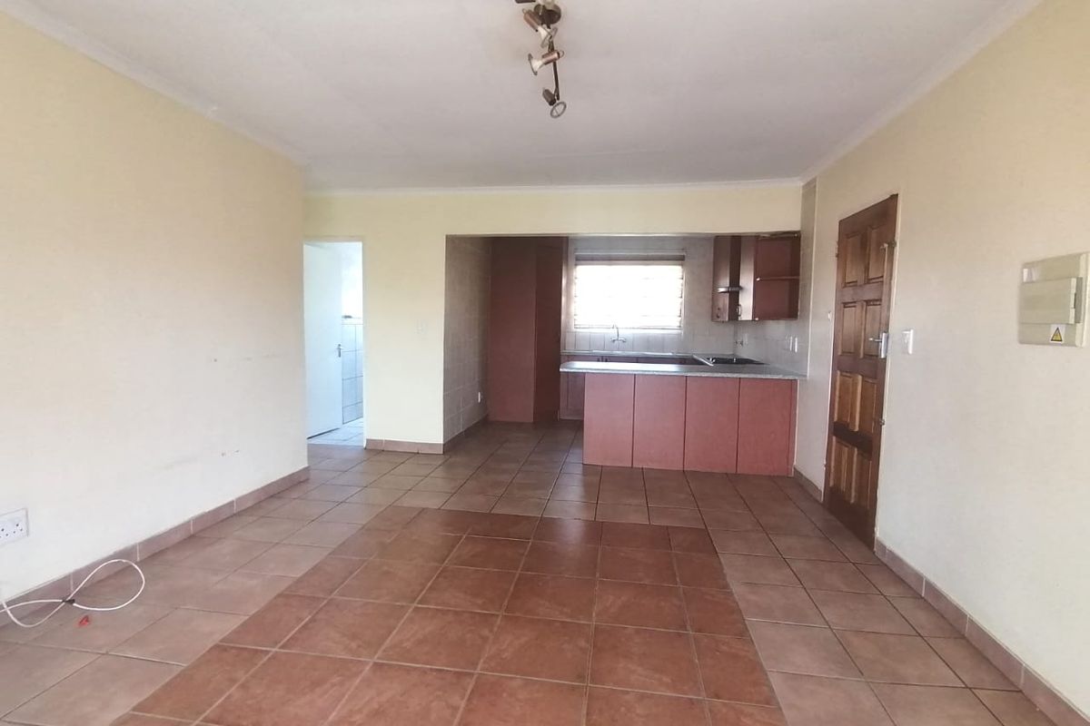 An open-plan living and kitchen area featuring tiled flooring, built-in cabinetry, and a central kitchen island, offering a functional blank canvas for renovation.