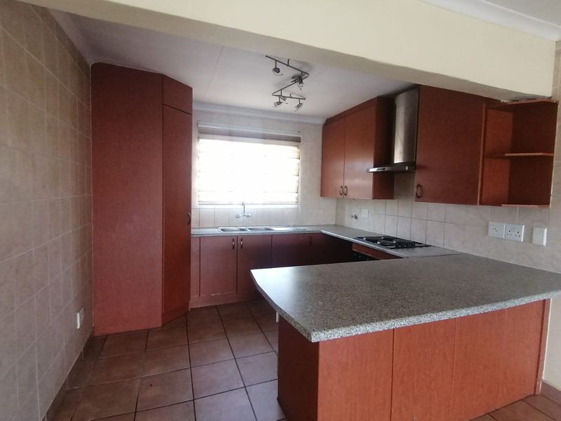 A functional kitchen featuring built-in cabinetry, a breakfast bar, stainless steel sink, and integrated hob with extractor fan, finished with tiled flooring and backsplash.