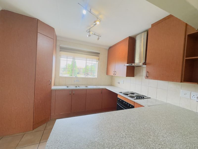 A functional kitchen featuring wood-tone cabinetry, laminate countertops, a double sink, and built-in cooking appliances with a tiled backsplash.