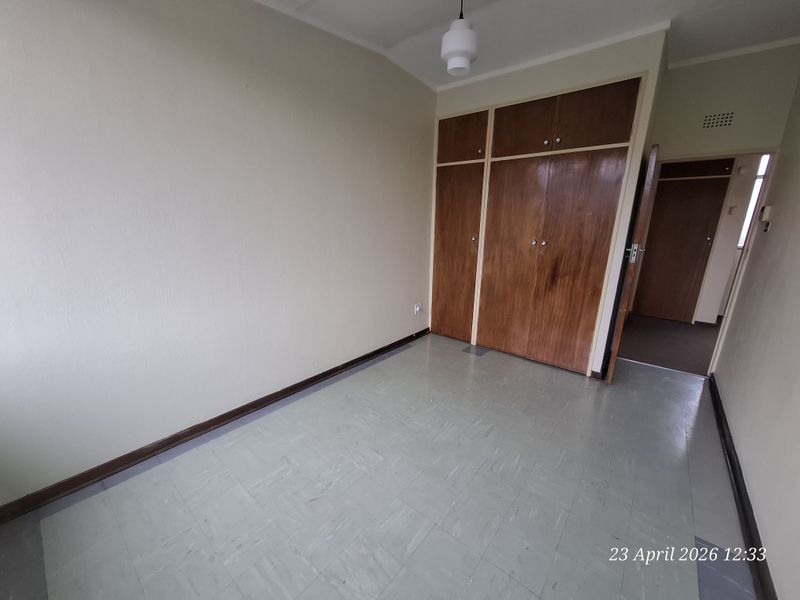 An empty bedroom featuring built-in wooden cupboards, vinyl tile flooring, and neutral wall finishes, offering a blank canvas for renovation.