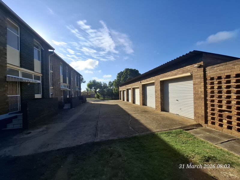 Exterior view of a townhouse complex featuring a row of garages, a concrete driveway, and brick building facades.