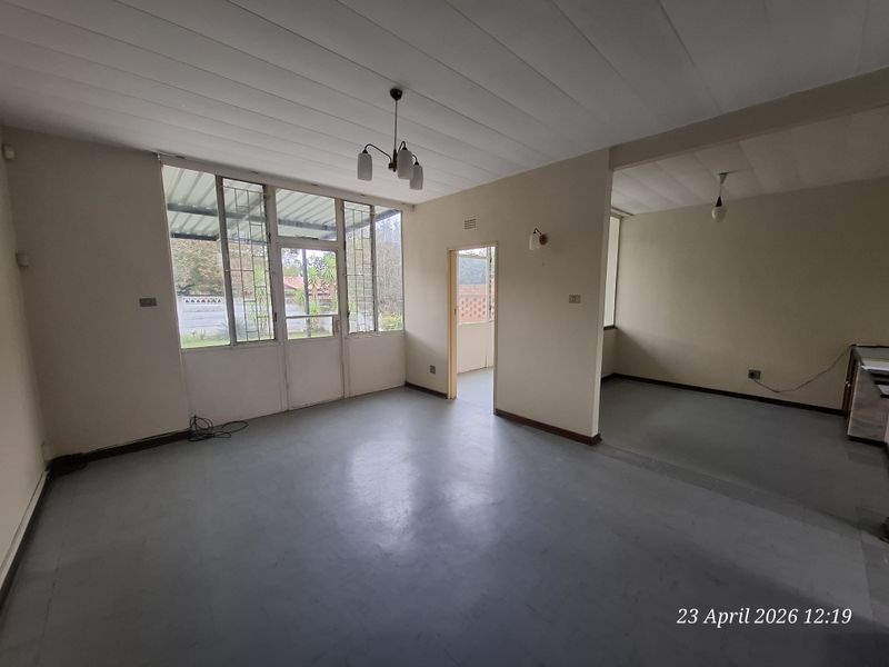Spacious open-plan living area featuring large windows, neutral walls, and direct access to the exterior, offering a blank canvas for renovation.