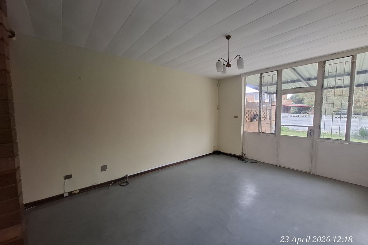 An empty living room featuring a glass panel door with security gate, neutral walls, and a simple ceiling light fixture.