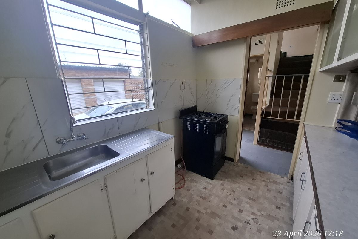 A dated kitchen featuring a stainless steel sink, gas stove, and original cabinetry, with direct access to an internal staircase.