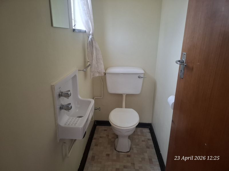 A compact guest bathroom featuring a wall-mounted basin and a standard close-coupled toilet with dated finishes.