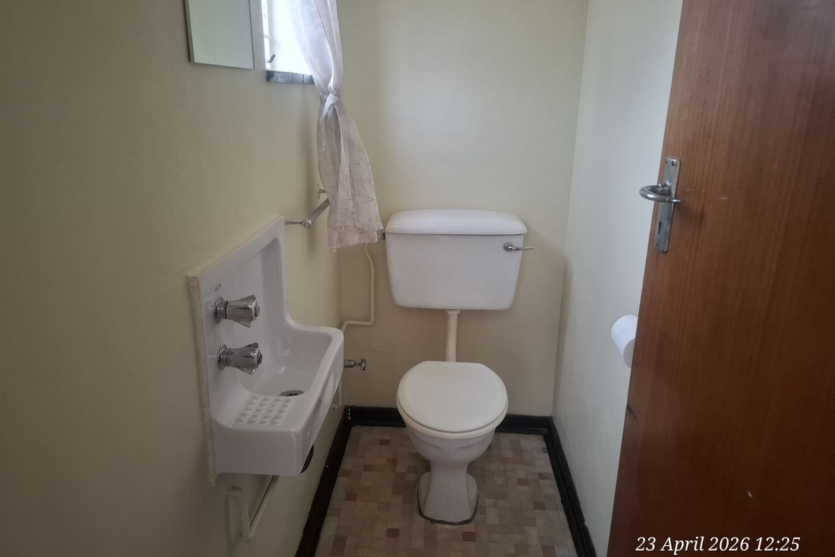 A compact guest bathroom featuring a wall-mounted basin and a standard close-coupled toilet with dated finishes.