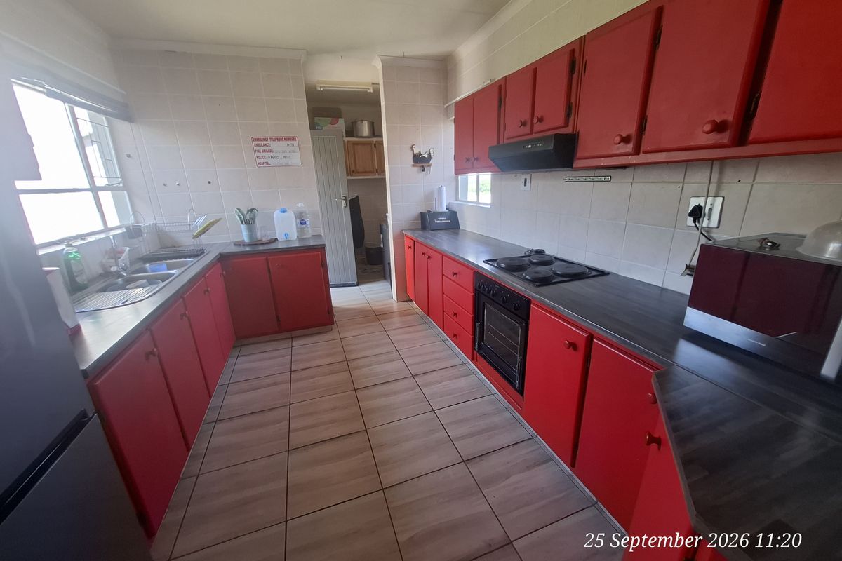 A functional kitchen featuring red cabinetry, laminate countertops, built-in oven, electric hob, and tiled flooring with a separate scullery area.
