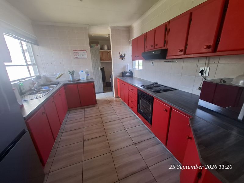 A functional kitchen featuring red cabinetry, laminate countertops, built-in oven, electric hob, and tiled flooring with a separate scullery area.