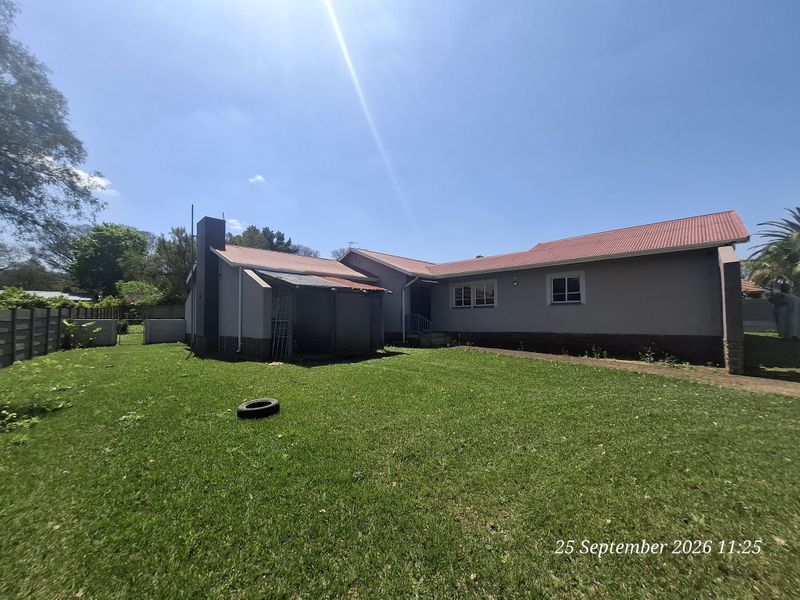 Rear view of the house featuring a corrugated metal roof, brick chimney, and a covered patio area set within a spacious garden.