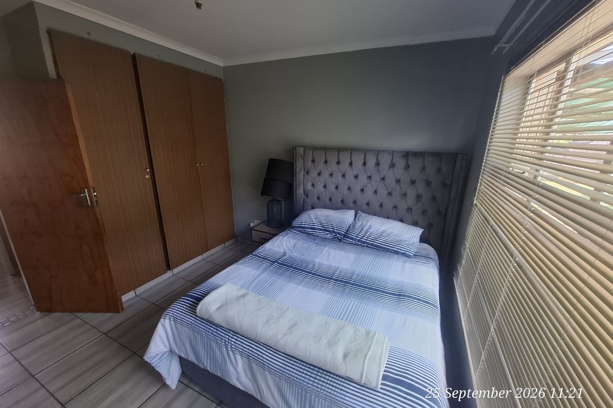 A functional bedroom featuring built-in wooden cupboards, tiled flooring, and venetian blinds, providing a neutral space ready for personalization.
