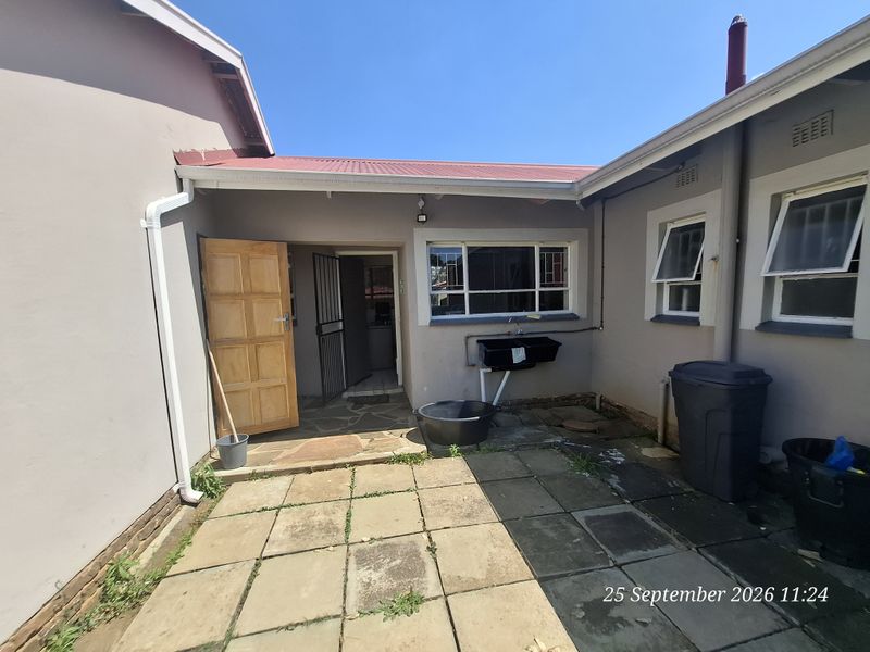 Rear courtyard area featuring paved flooring, an external utility sink, and access to the main dwelling via a timber door and security gate.
